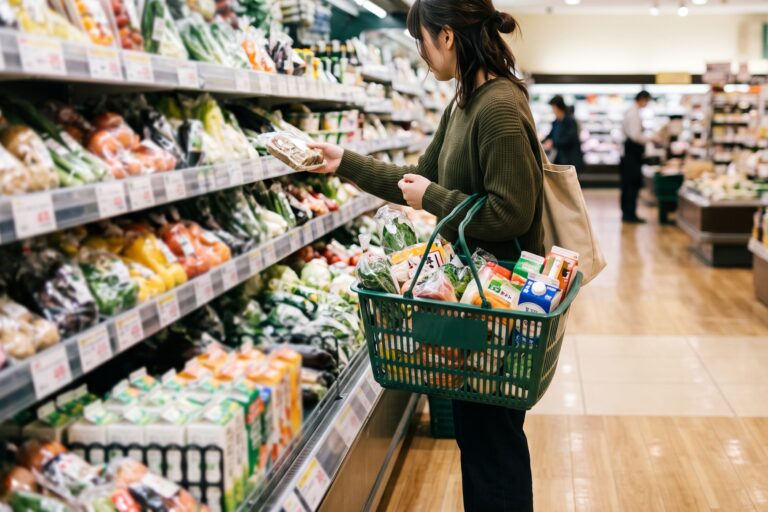 スーパーで買い物カゴを持ち商品を手に取る買い物客